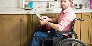 A man in a wheelchair is cleaning at a kitchen sink, demonstrating independence and engagement in household tasks.