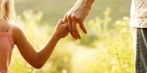 A young girl holds the hand of an adult, symbolizing guidance and support in a nurturing relationship.