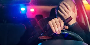 A man sitting in the driver's seat of a car, looking stressed with his hands on his head.