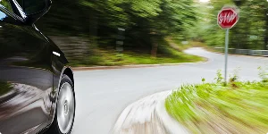 A car speeds recklessly on a winding road with a stop sign, navigating sharp turns that resemble waves.