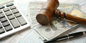 A court gavel rests on $100 bills beside a calculator and tax-related papers, symbolizing tax preparation services