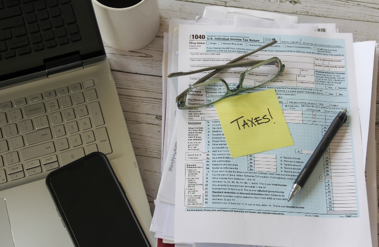 laptop beside tax documents with yellow sticky note with the word taxes