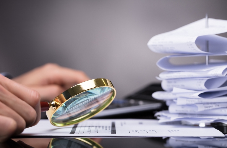 man looks at documents through a magnifying glass