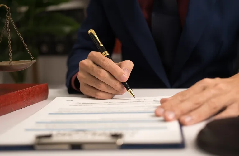 A person in a dark suit signing a document with a black and gold pen.