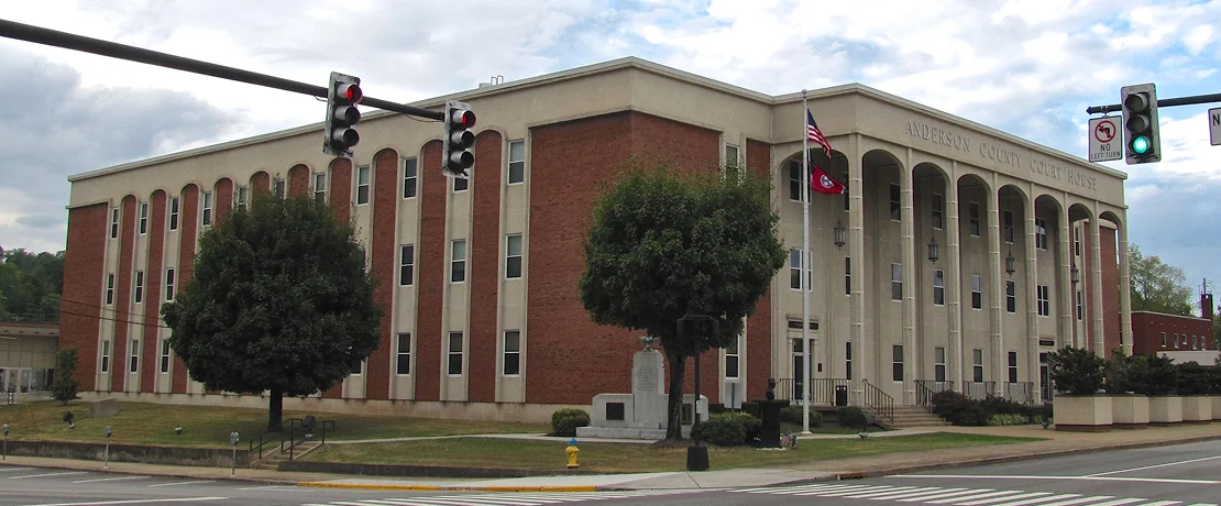 A big brick and stone courthouse with two flagpoles and traffic lights nearby.