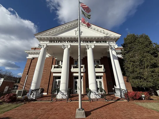 Big brick courthouse with tall white columns, flags flying, and a bright blue sky.
