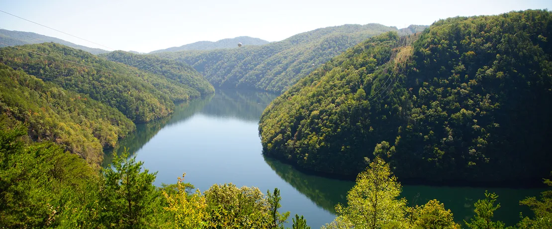 A chill river winding through green, tree-covered hills on a sunny day.