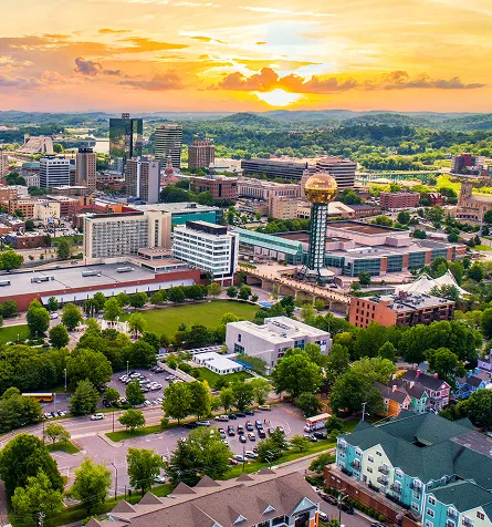 A colorful cityscape at sunset with a shiny gold globe tower and lots of green trees.