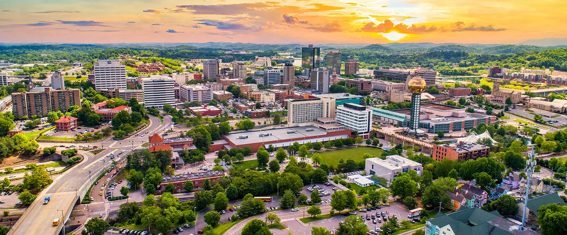 A colorful cityscape at sunset with buildings, greenery, and a shiny golden sphere tower.