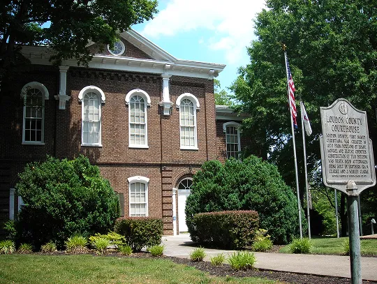 A sunny day at a brick courthouse with tall windows, green bushes, and flags.