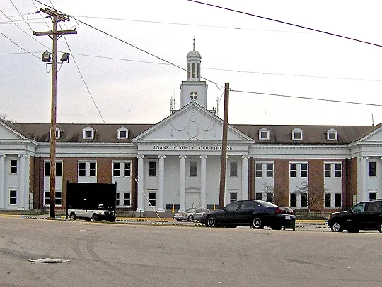 Front view of a classic courthouse building with white columns and parked cars nearby.