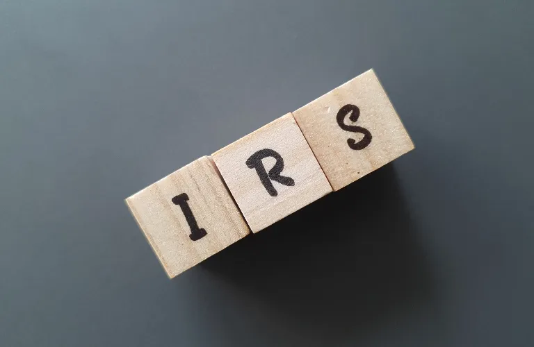Three wooden blocks with black letters I, R, and S on a gray background.