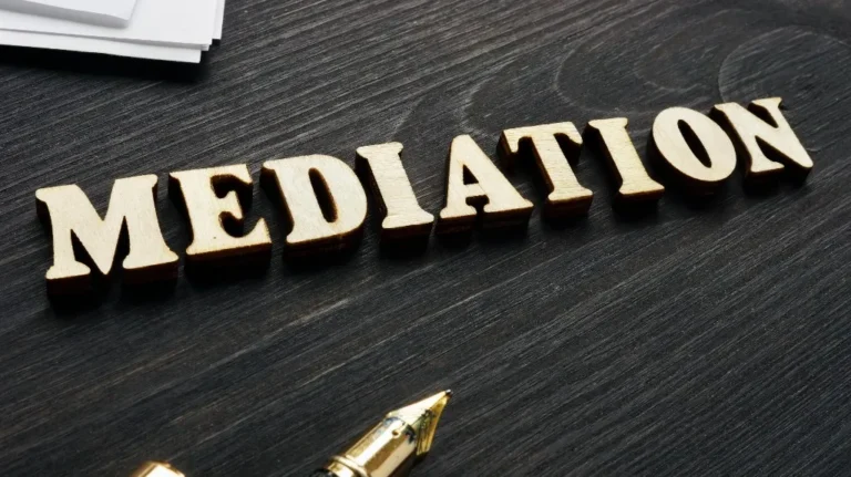 Wooden letters spelling "MEDIATION" on a dark wooden table with a gold pen nearby.