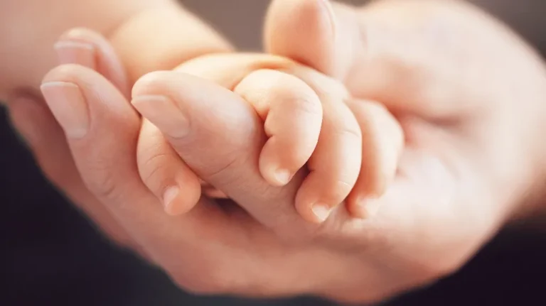 A tiny baby hand gently held in a larger adult hand, soft warm tones.