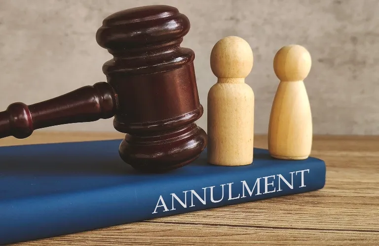 A wooden judge’s gavel, two wooden figures, and a blue book labeled “ANNULMENT.”