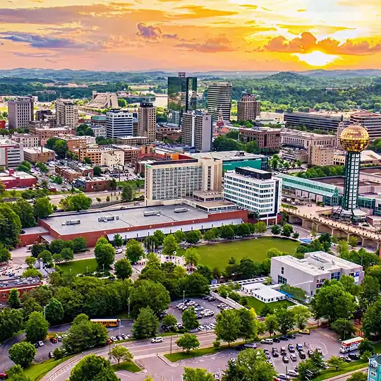 Sunny city skyline with tall buildings, green trees, and a glowing golden globe tower at sunset.