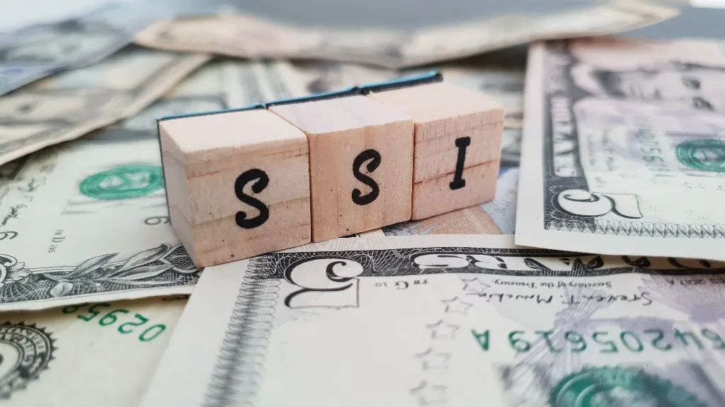 Wooden blocks spelling "SSI" resting on scattered US dollar bills.