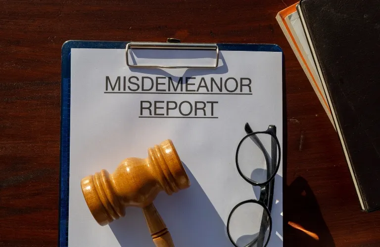 A clipboard with a "Misdemeanor Report" paper, wooden gavel, and black glasses.
