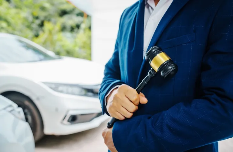 Person in a blue suit holding a black and gold auction gavel near white cars.