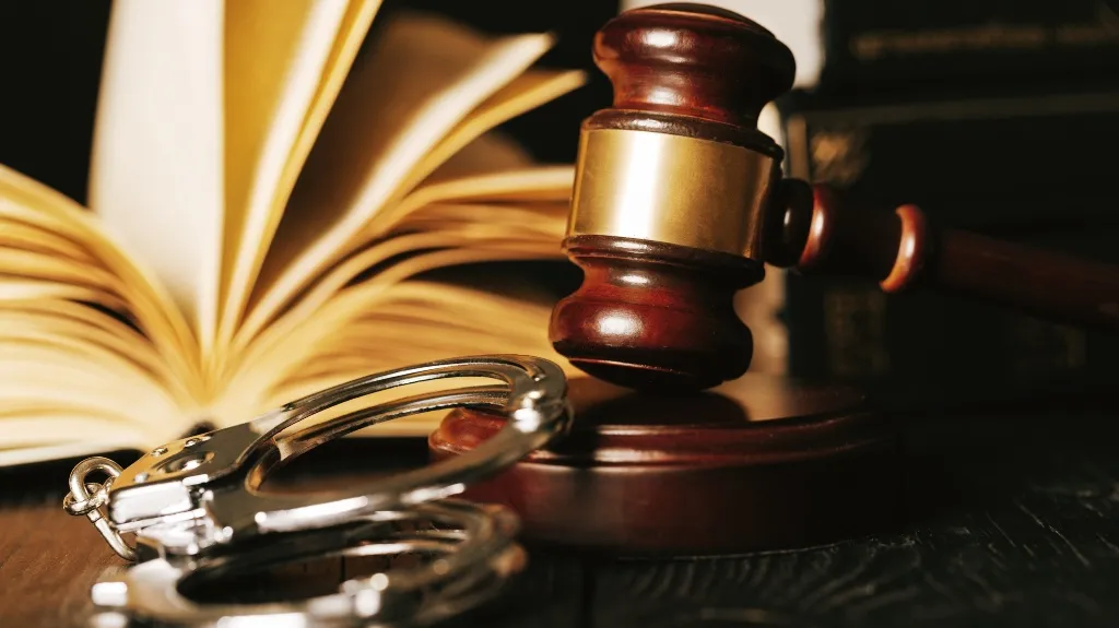 A wooden judge's gavel, shiny silver handcuffs, and an open book with yellowed pages.