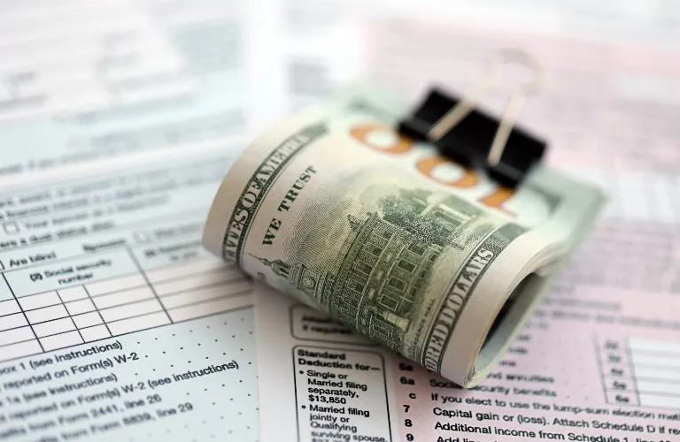 Rolled hundred-dollar bill clipped on tax forms with printed text.