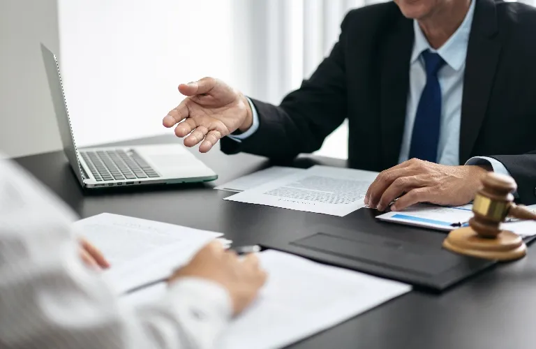 Two people discussing documents at a desk with a laptop and judge’s gavel.