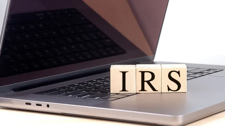 Wooden blocks spelling IRS sitting on a sleek gray laptop keyboard.