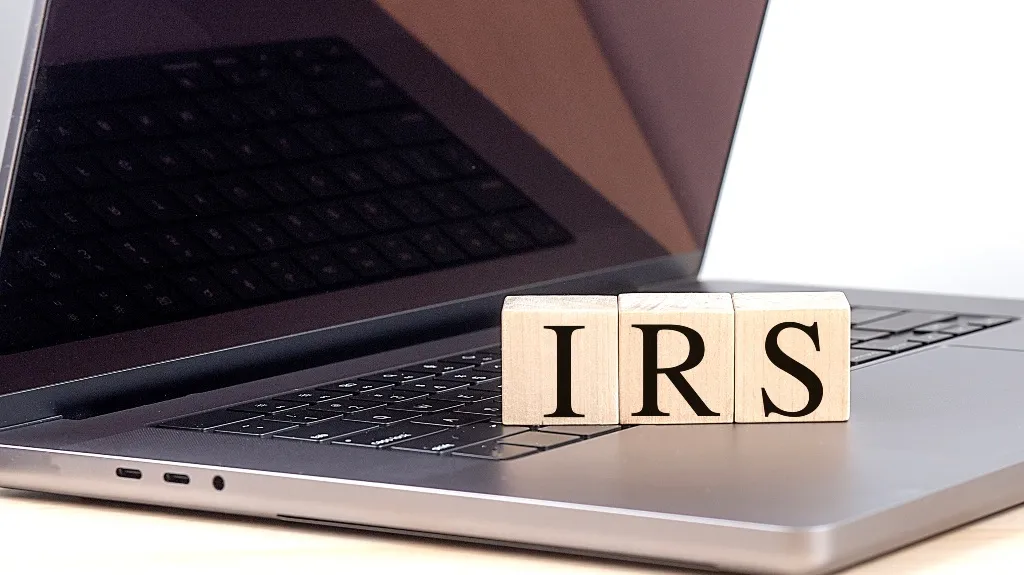 Wooden blocks spelling IRS sitting on a sleek gray laptop keyboard.