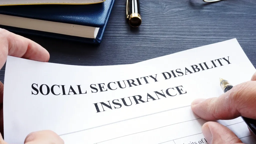 Hands holding a Social Security Disability Insurance form with a pen nearby.