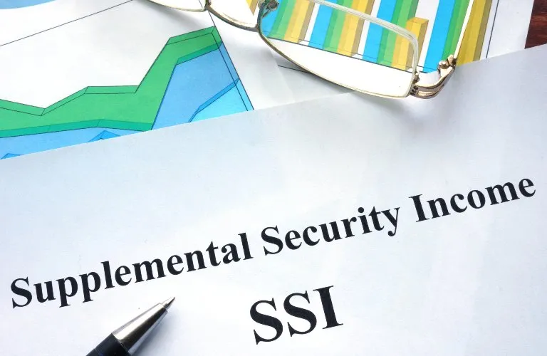 A close-up of a paper titled "Supplemental Security Income SSI" with colorful charts, glasses, and a pen nearby.