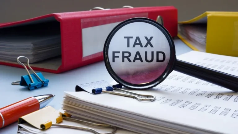Magnifying glass highlighting "TAX FRAUD" over paperwork with colorful binders and clips nearby.