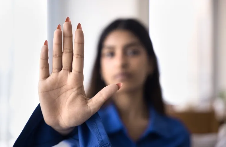 A person in a blue shirt holding up their hand toward the camera, palm facing forward.