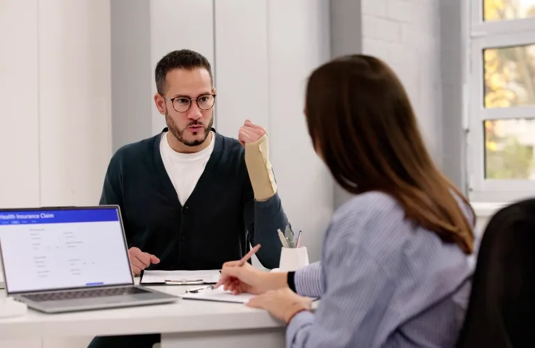 Two people chatting at a desk with a laptop showing a health insurance claim form.