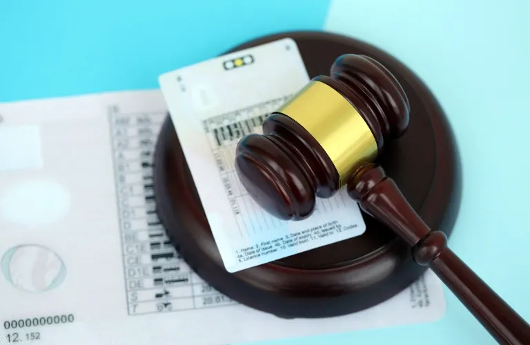 A wooden judge’s gavel resting on a driver’s license on a bright blue background.