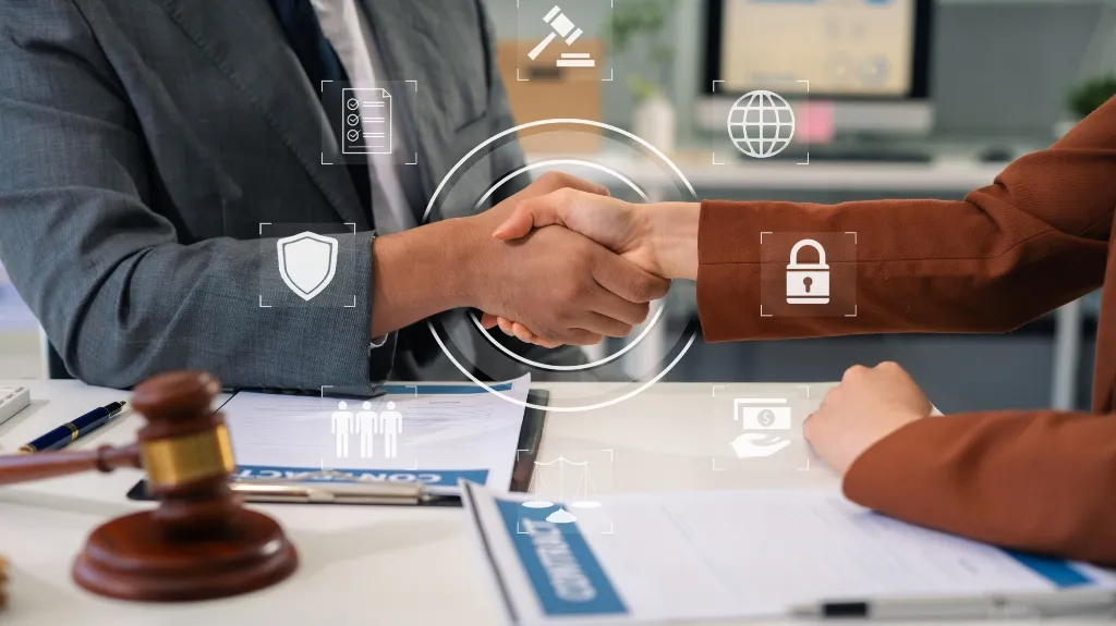 Two people shaking hands over a desk with legal documents and a gavel nearby.