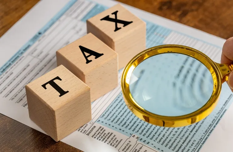 Wooden blocks spelling "TAX" next to a gold-rimmed magnifying glass on a tax form.