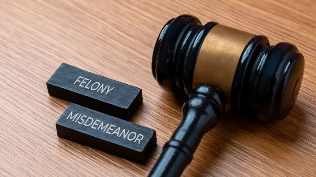 A black judge’s gavel next to wooden blocks labeled Felony and Misdemeanor on a table.