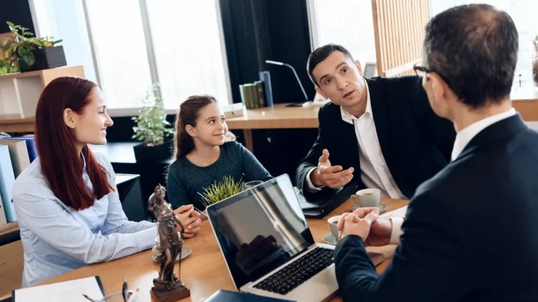 Four people chatting around a wooden table with a laptop and coffee cups.