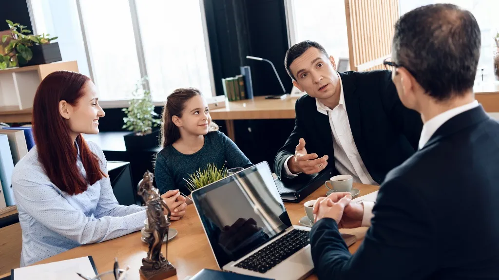 Four people chatting around a wooden table with a laptop and coffee cups.