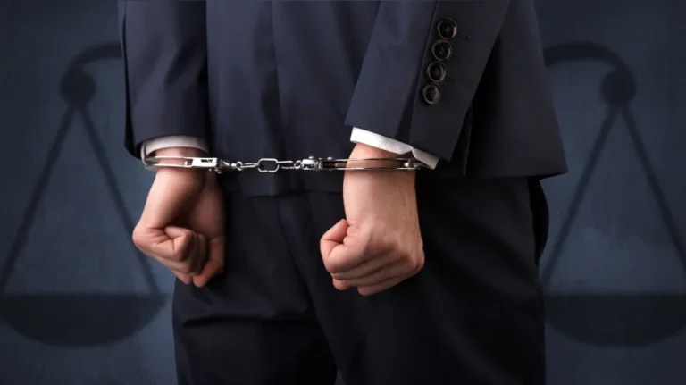 Person in dark suit with hands cuffed behind back, shadow of scales in background.