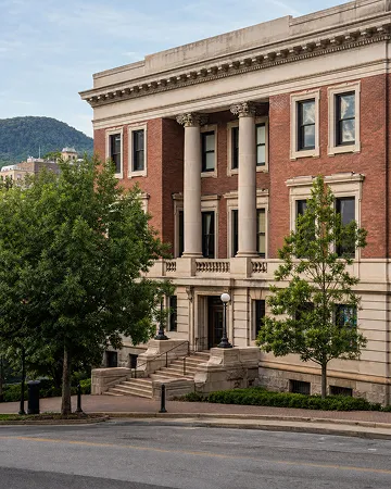 A red brick building with tall columns, trees, and a mountain in the background.