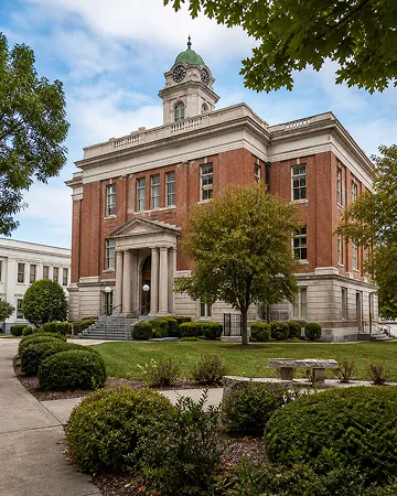 Classic red brick courthouse with a clock tower, surrounded by green trees and bushes.