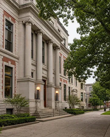 A grand old building with tall columns, glowing lamps, and leafy trees lining the sidewalk.