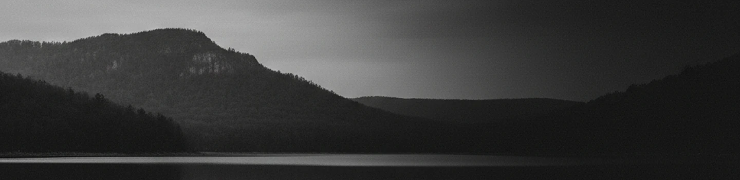A calm lake at night with dark forested hills and a cloudy sky.