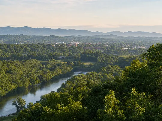 A peaceful river winding through lush green trees with distant blue mountains.
