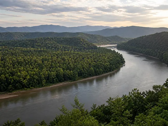 A calm river winding through lush green hills under a cloudy sky.