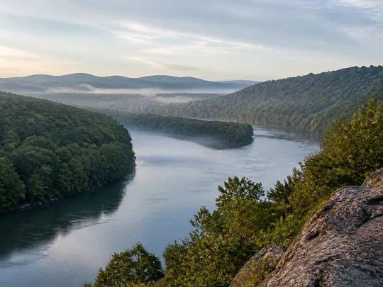 Chill river winding through lush green hills with misty morning vibes.