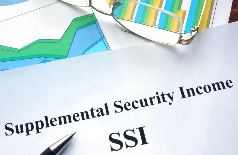 A close-up of a paper titled “Supplemental Security Income SSI” with a pen and colorful reading glasses nearby.