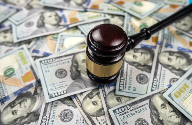 A dark wooden judge’s gavel resting on a pile of hundred-dollar bills.